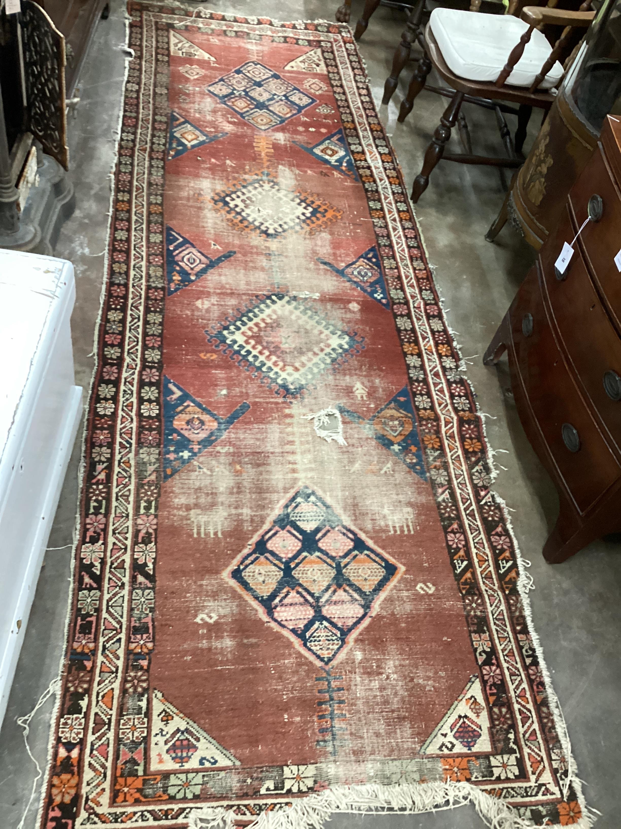 An Antique Caucasian brick red ground runner 336cm x 110cm, severely worn and holed